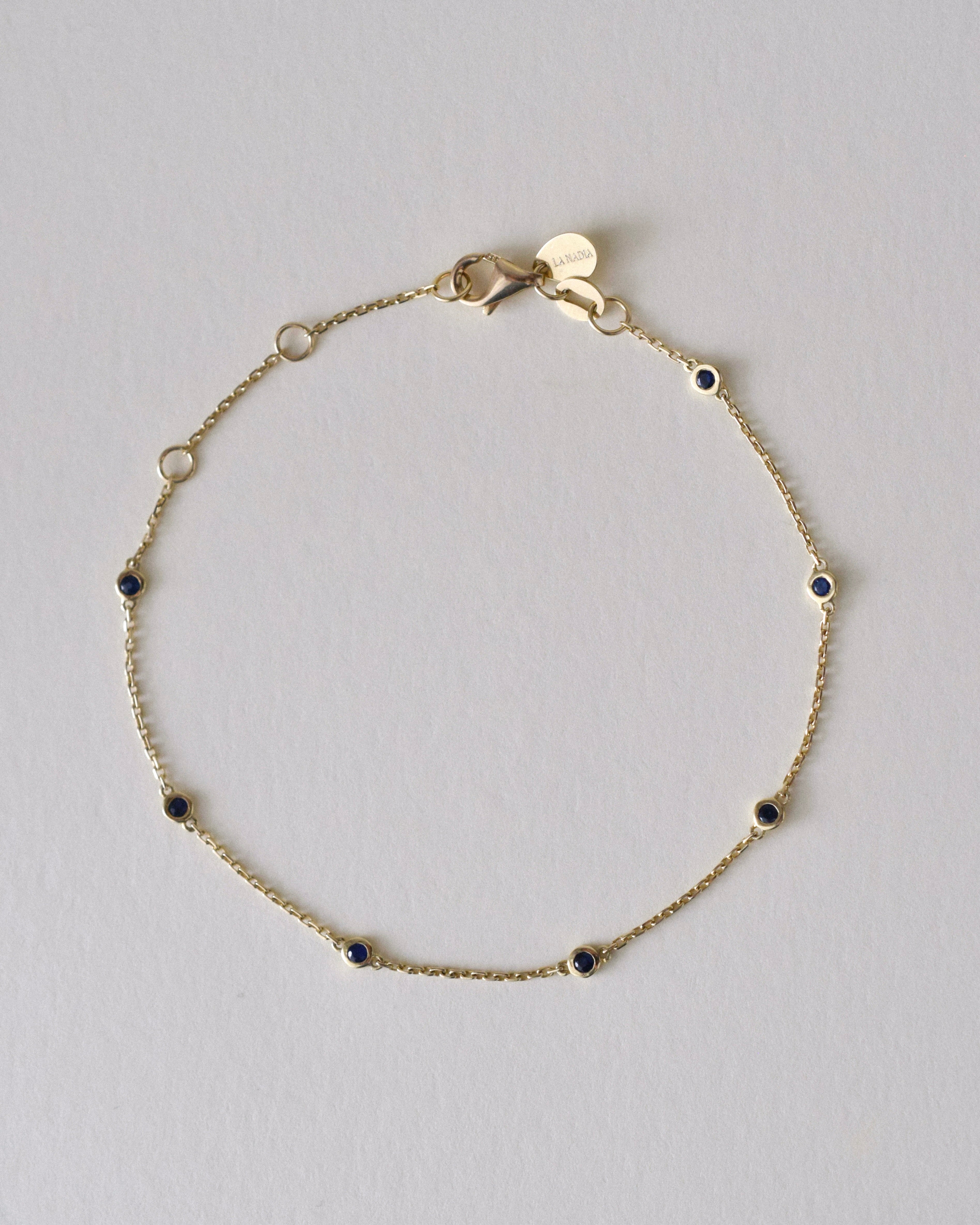 Gold bracelet with small blue sapphire gemstones on a light gray background