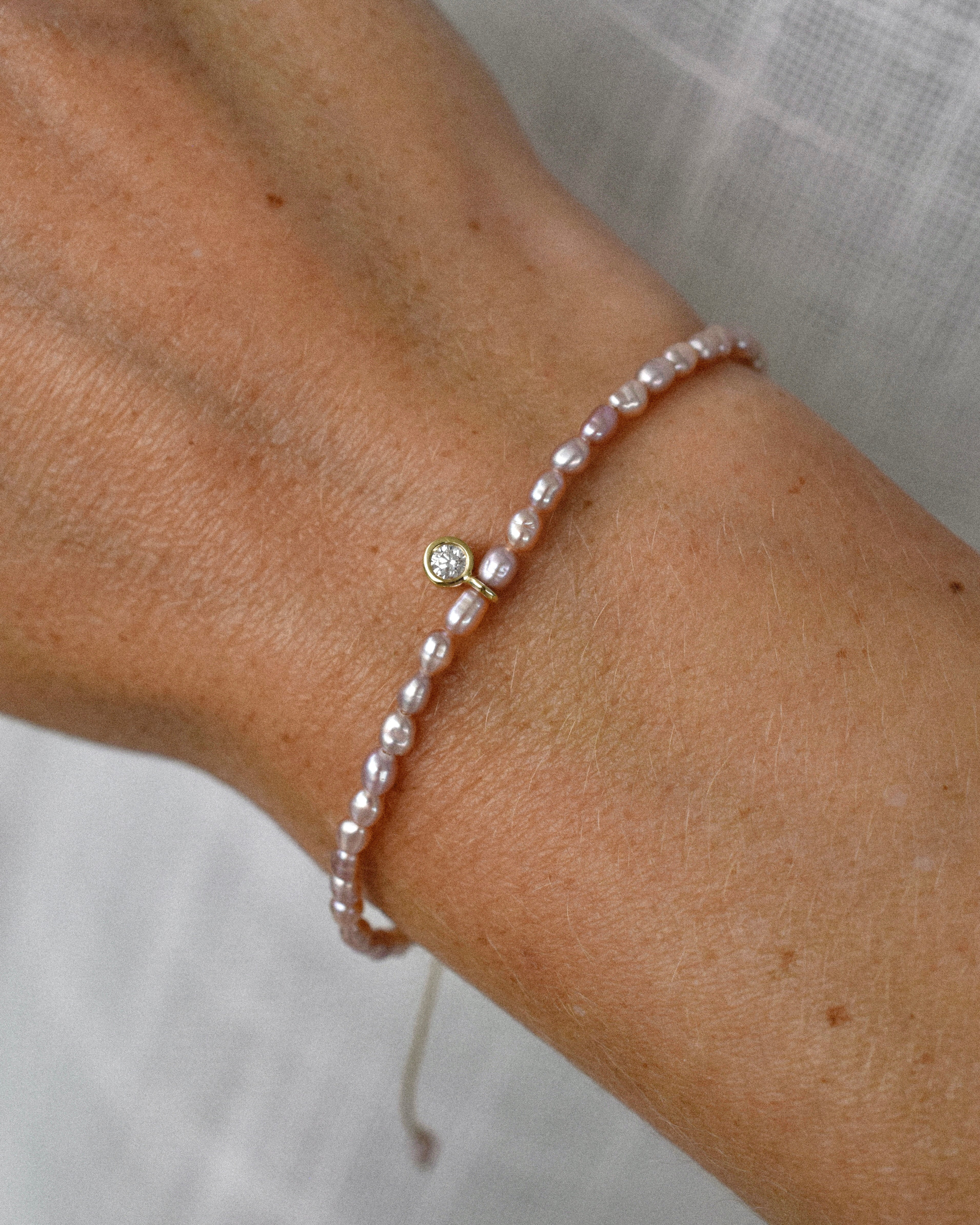 Pearl bracelet with purple pearls and a diamond solitaire charm on a wrist against a neutral background