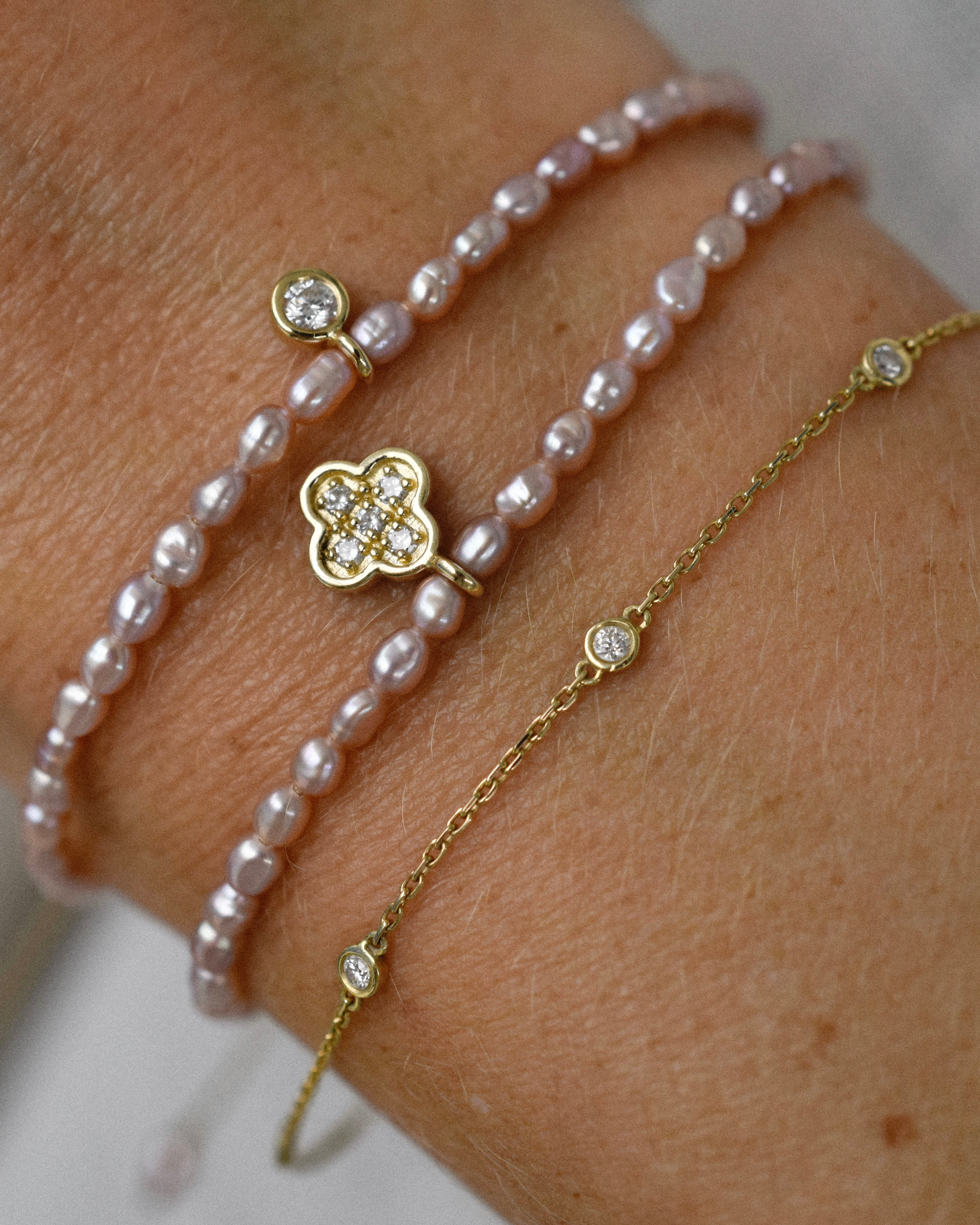 Close-up of a wrist wearing a gold bracelet with diamonds and two pearl bracelets.