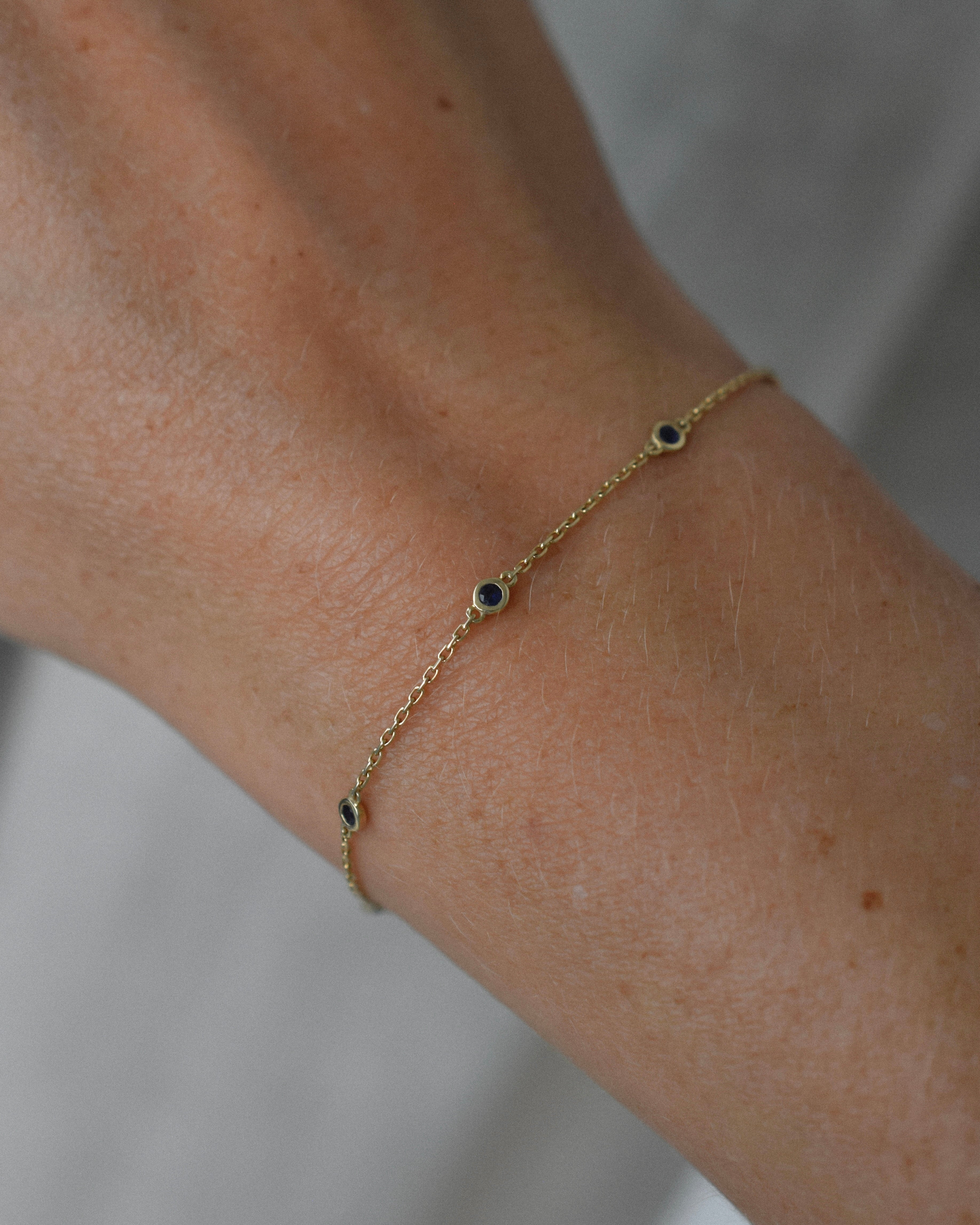 Gold bracelet with small sapphire stones on a wrist against a neutral background