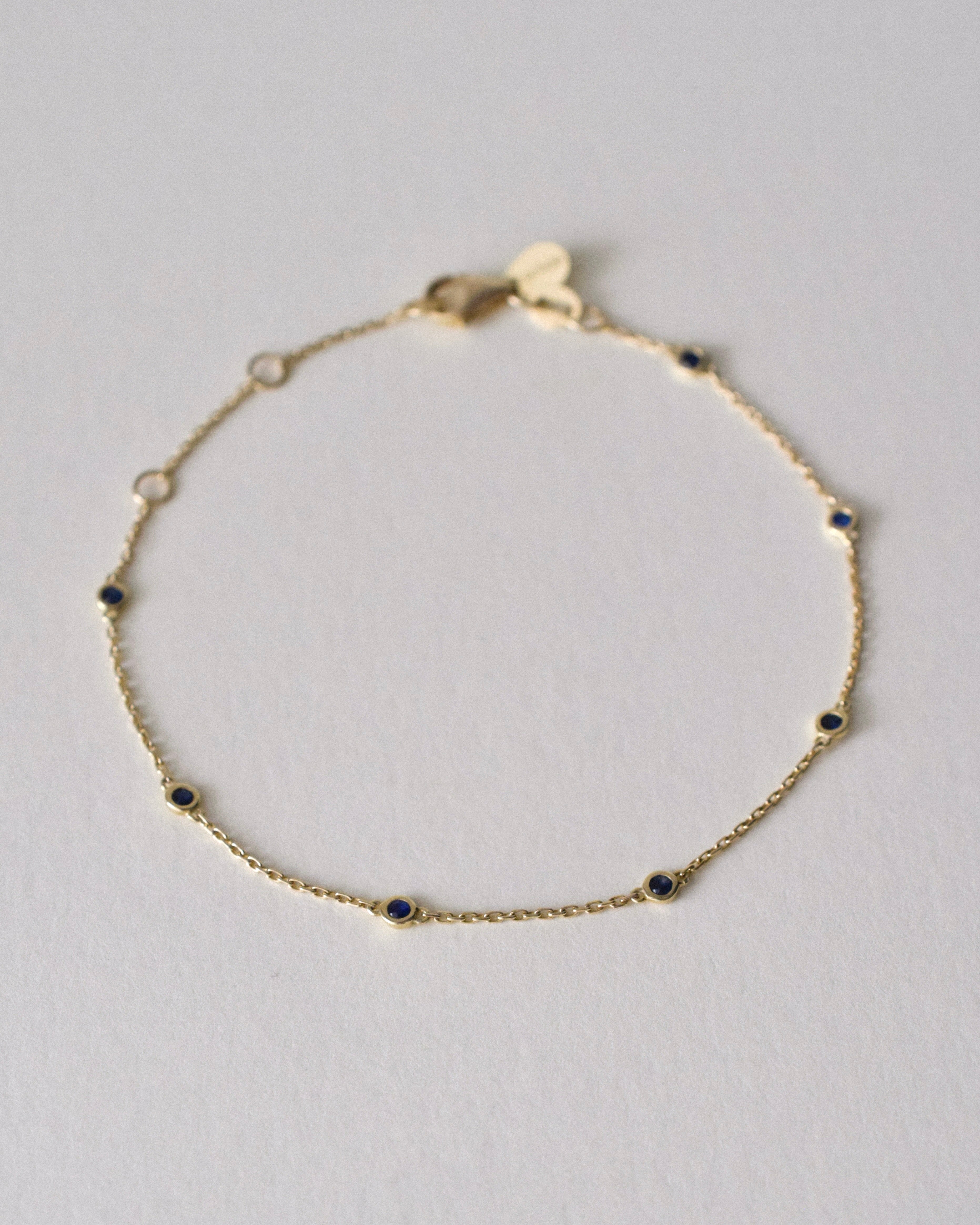 Gold bracelet with small blue sapphire gemstones on a light gray background