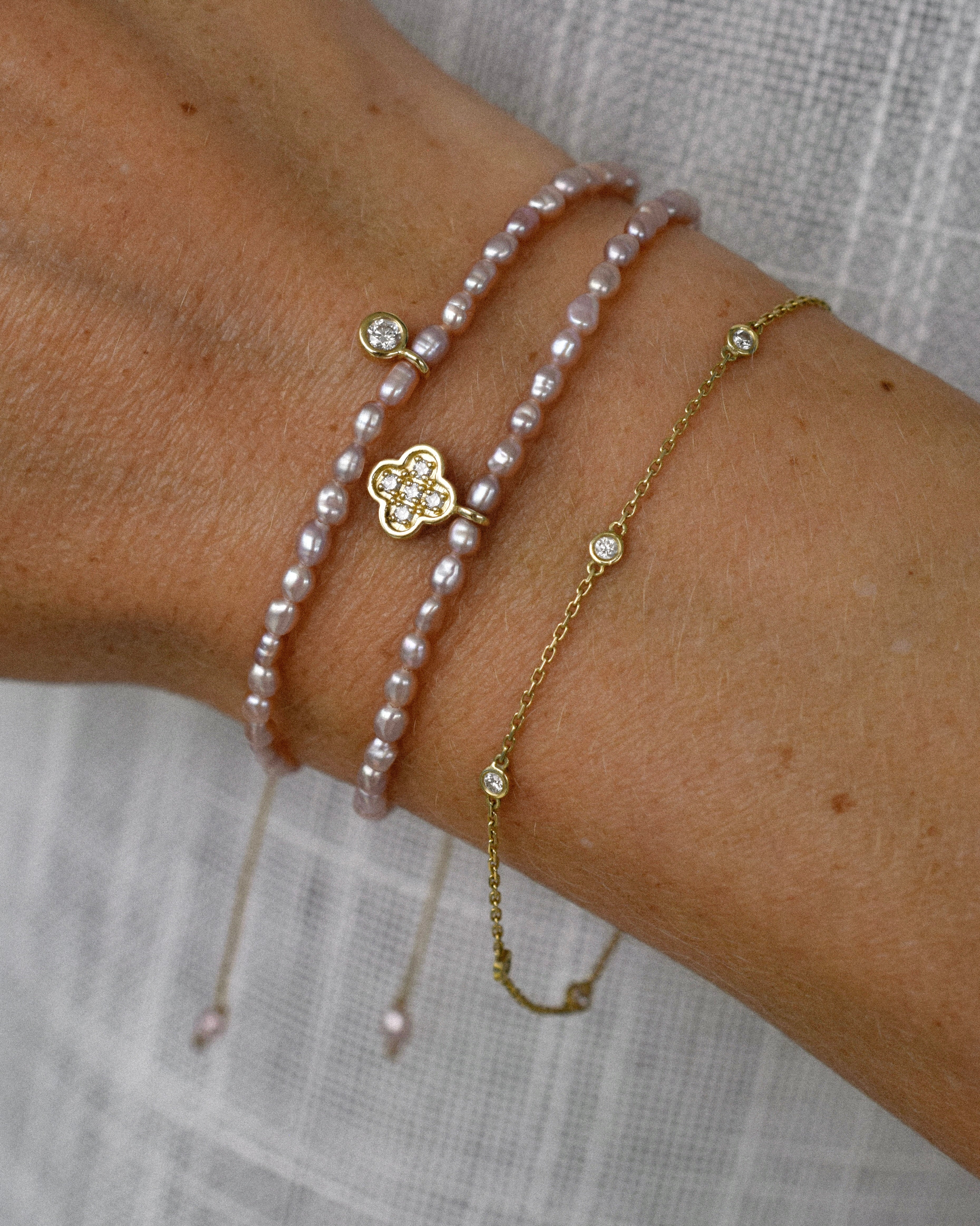 Close-up of a wrist wearing multiple pearl and gold bracelets on a neutral background