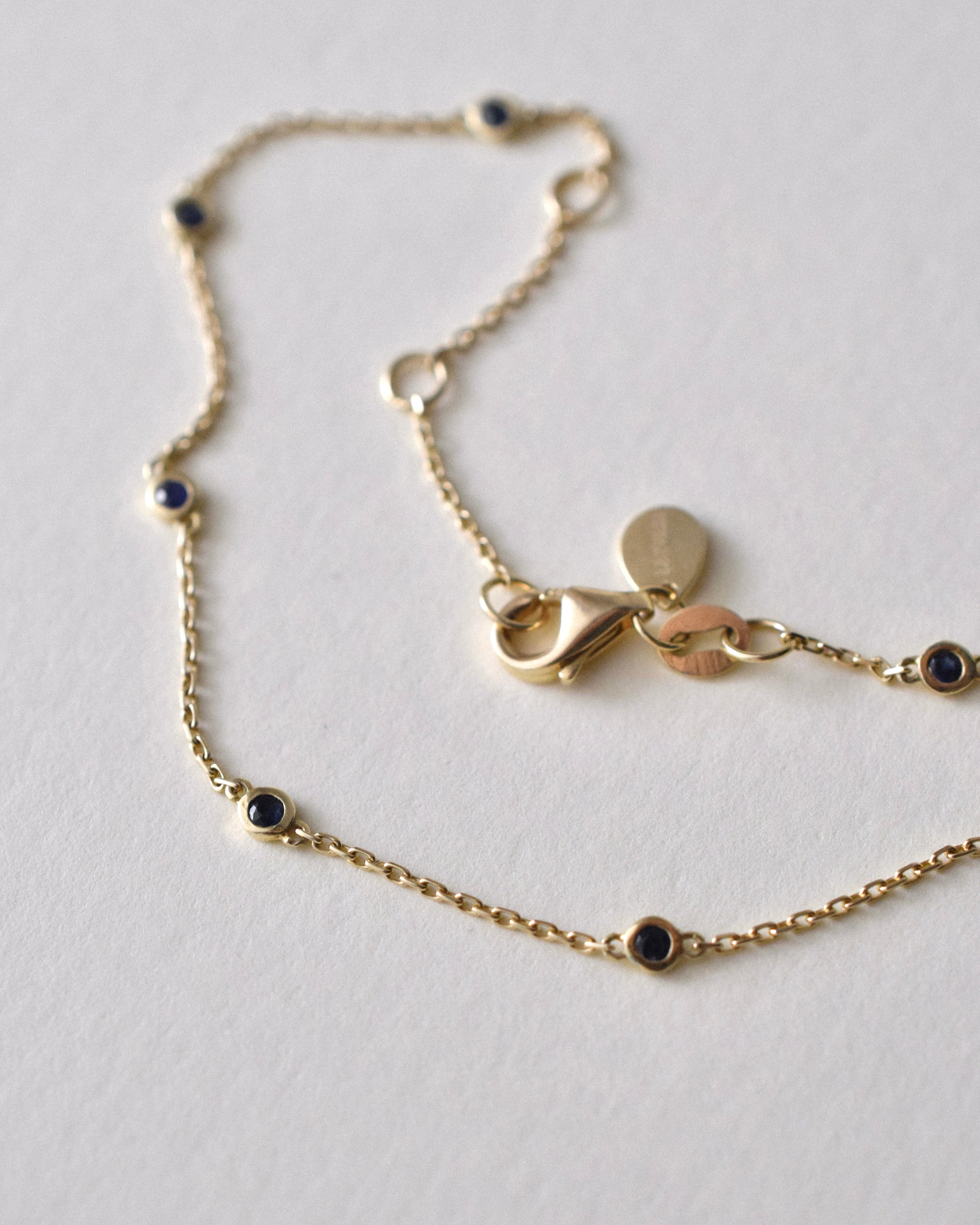 Gold bracelet with round blue sapphire charms on a light gray background