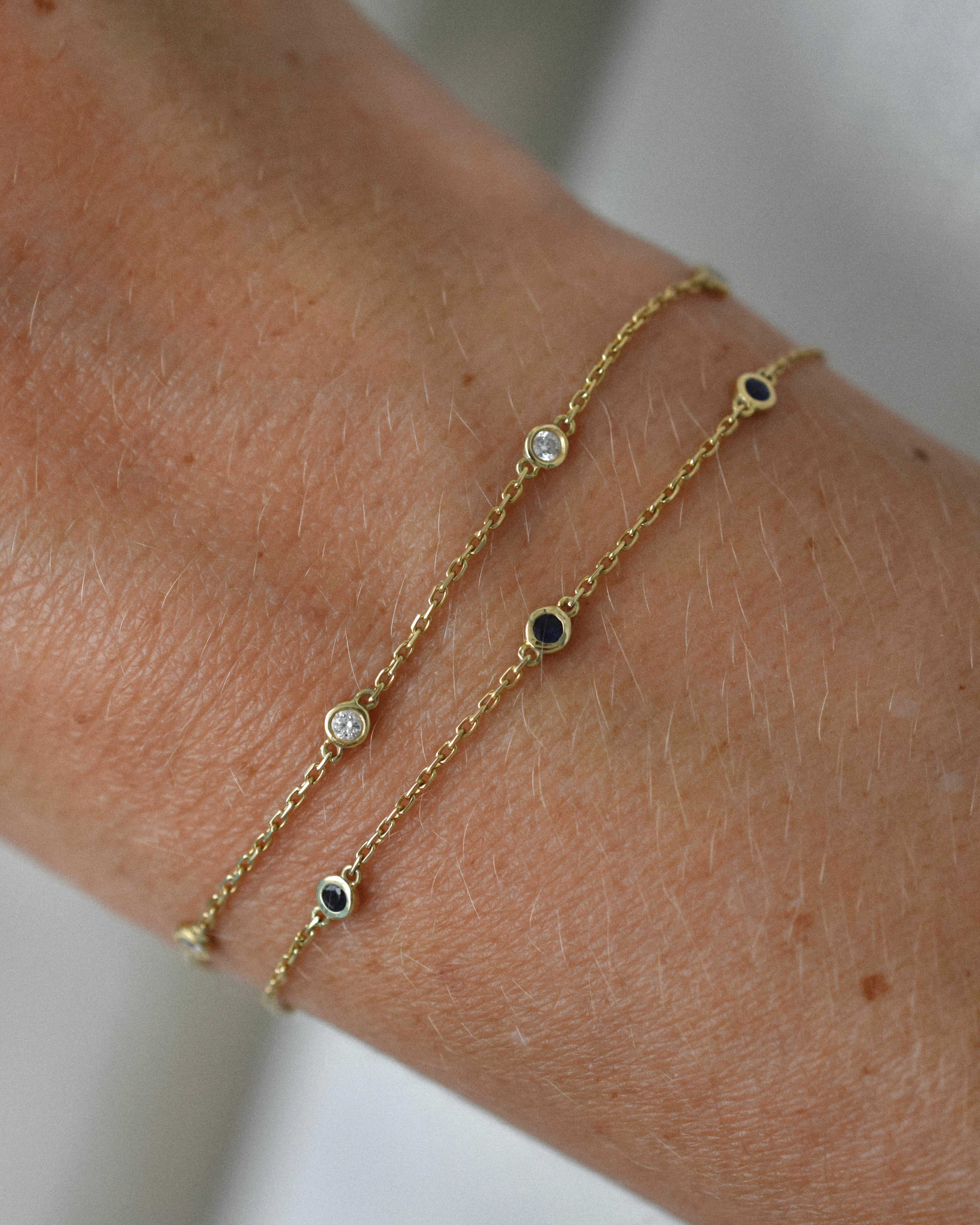 Two gold bracelets with diamonds and sapphire gemstones on a wrist against a neutral background