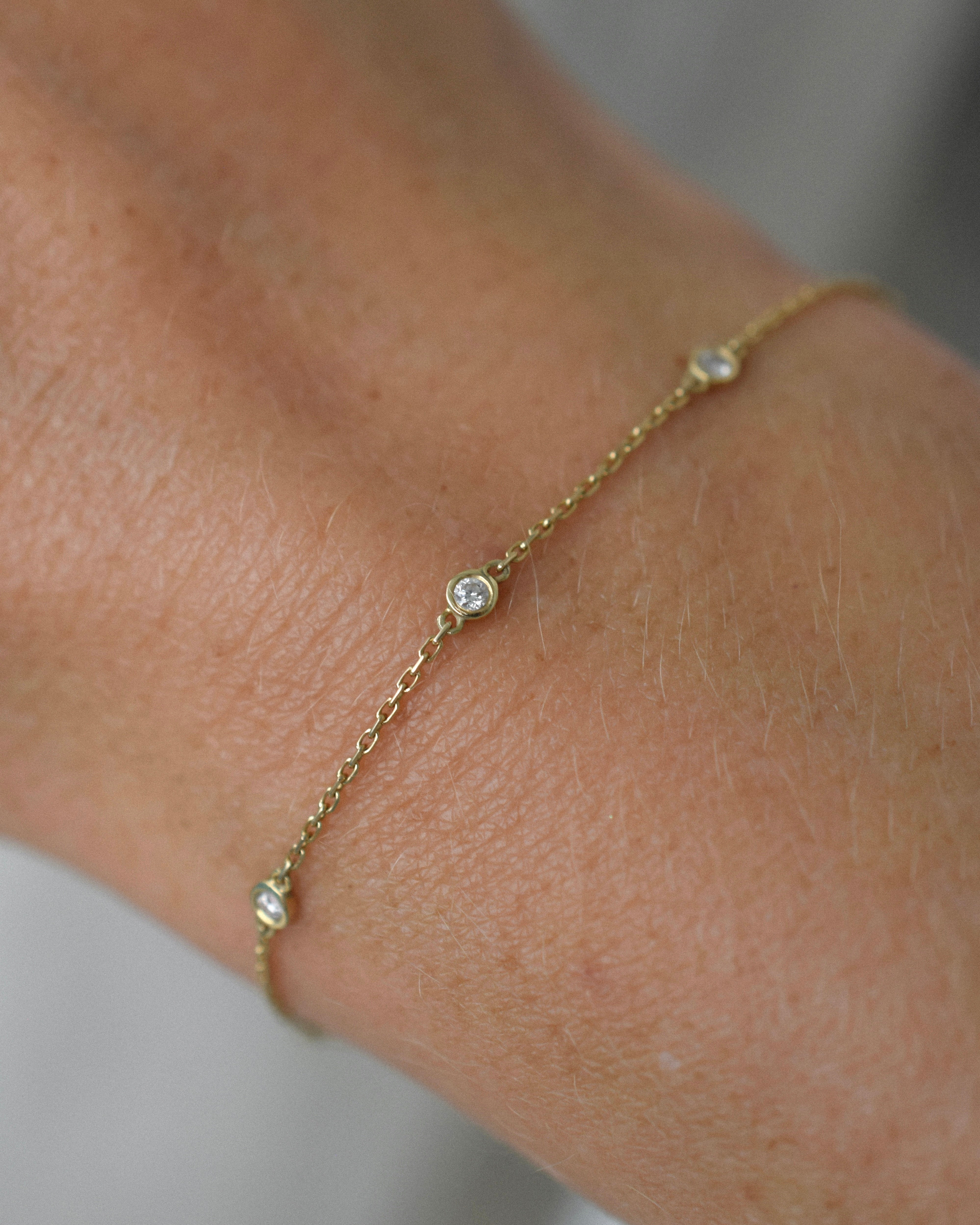 Gold bracelet with small stones on a wrist against a neutral background