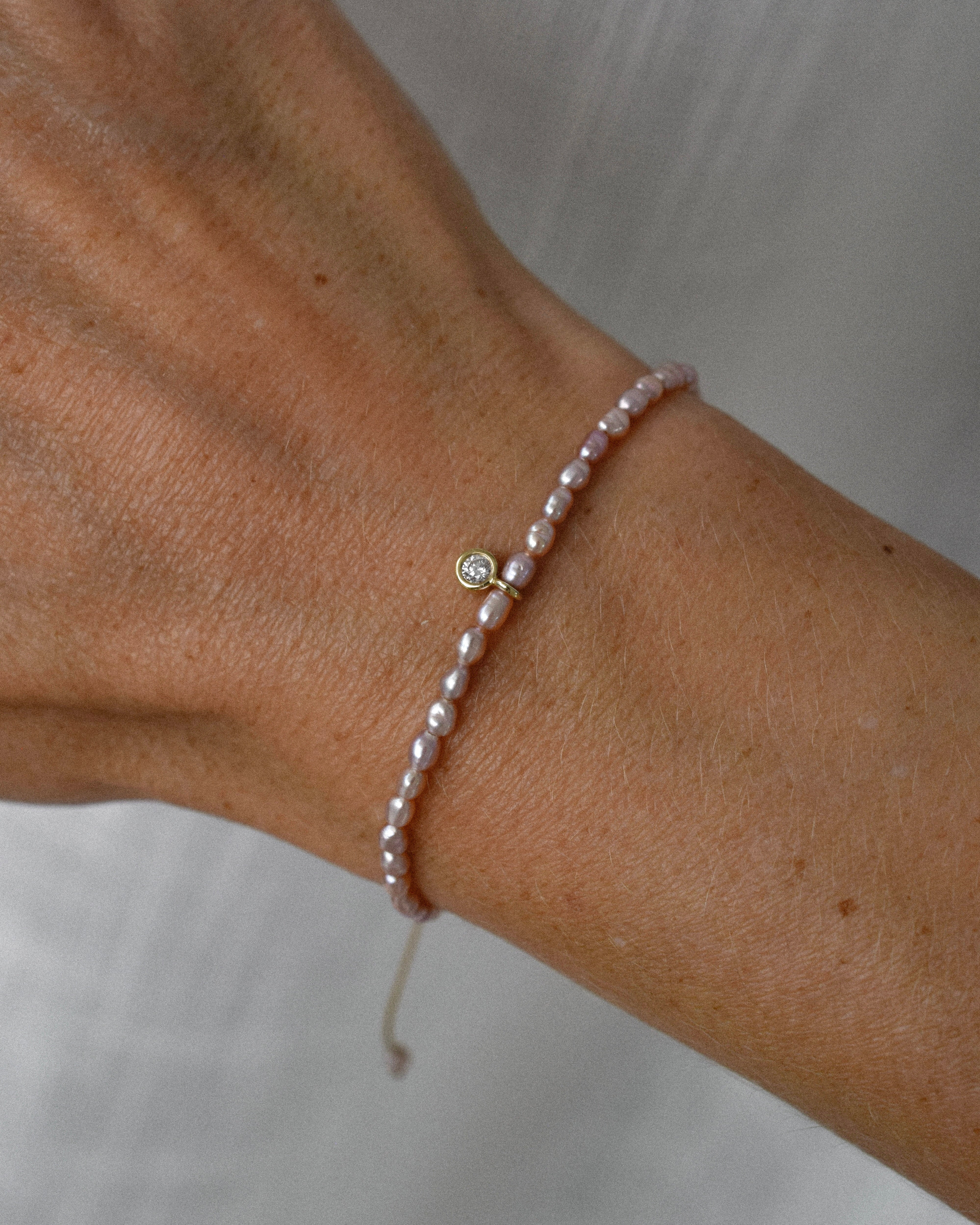 Pearl bracelet with purple pearls and a diamond solitaire charm on a wrist against a neutral background