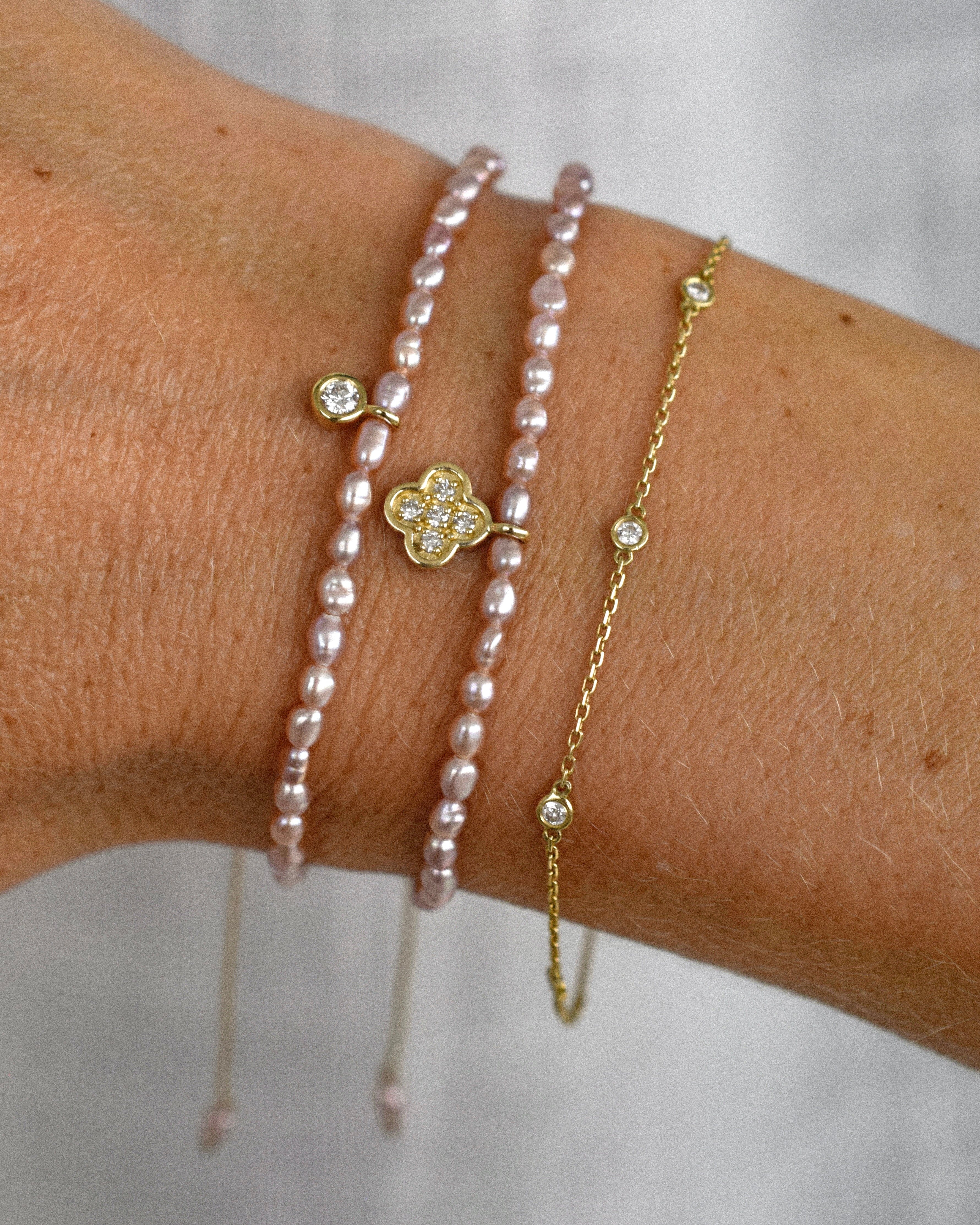 Two pearl bracelets and a gold chain bracelet with diamonds on a wrist against a white background