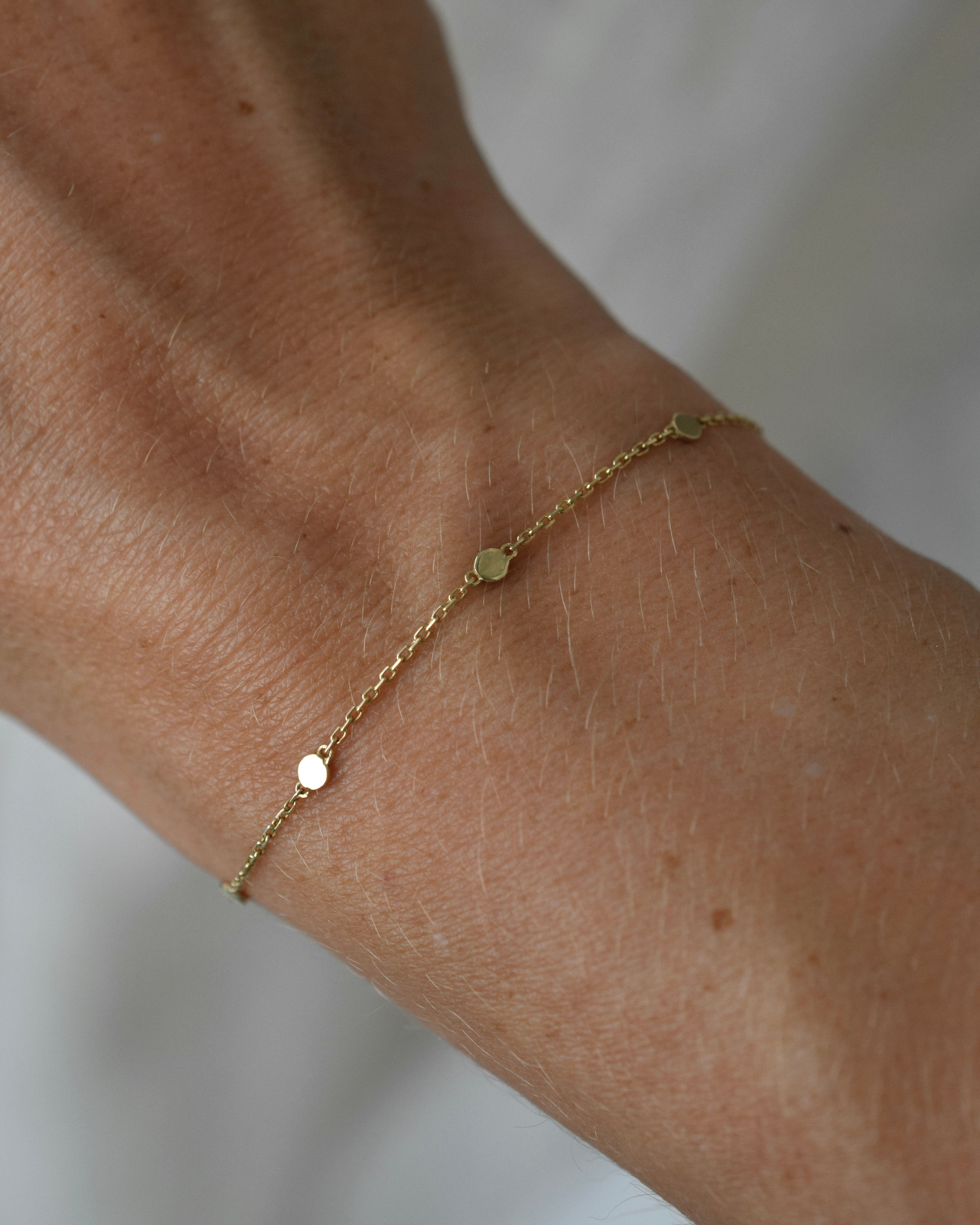Gold bracelet on a wrist with a plain background