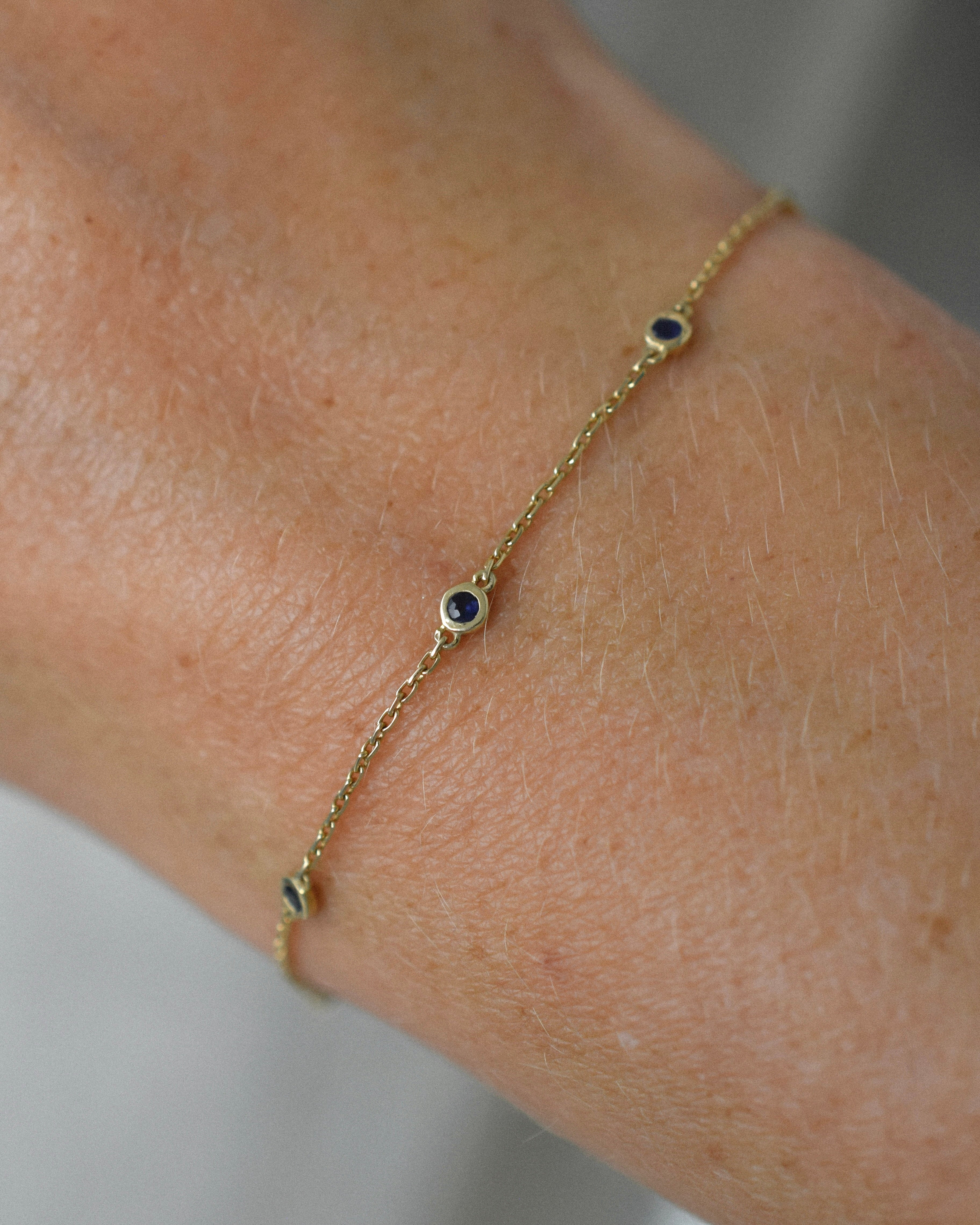 Gold bracelet with blue sapphire stones on a wrist against a neutral background