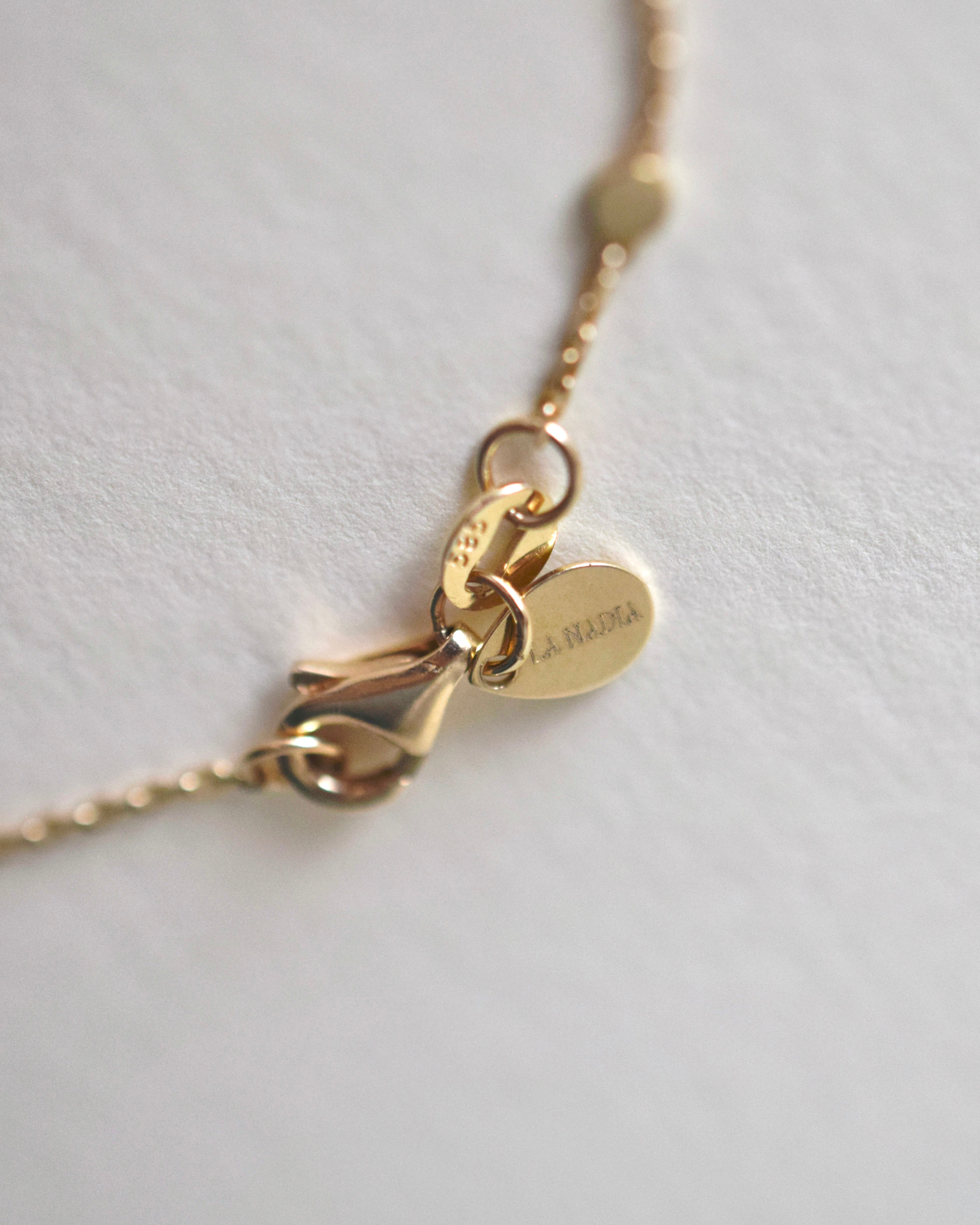 Gold necklace with a lobster clasp and jewelry tag on a light gray background