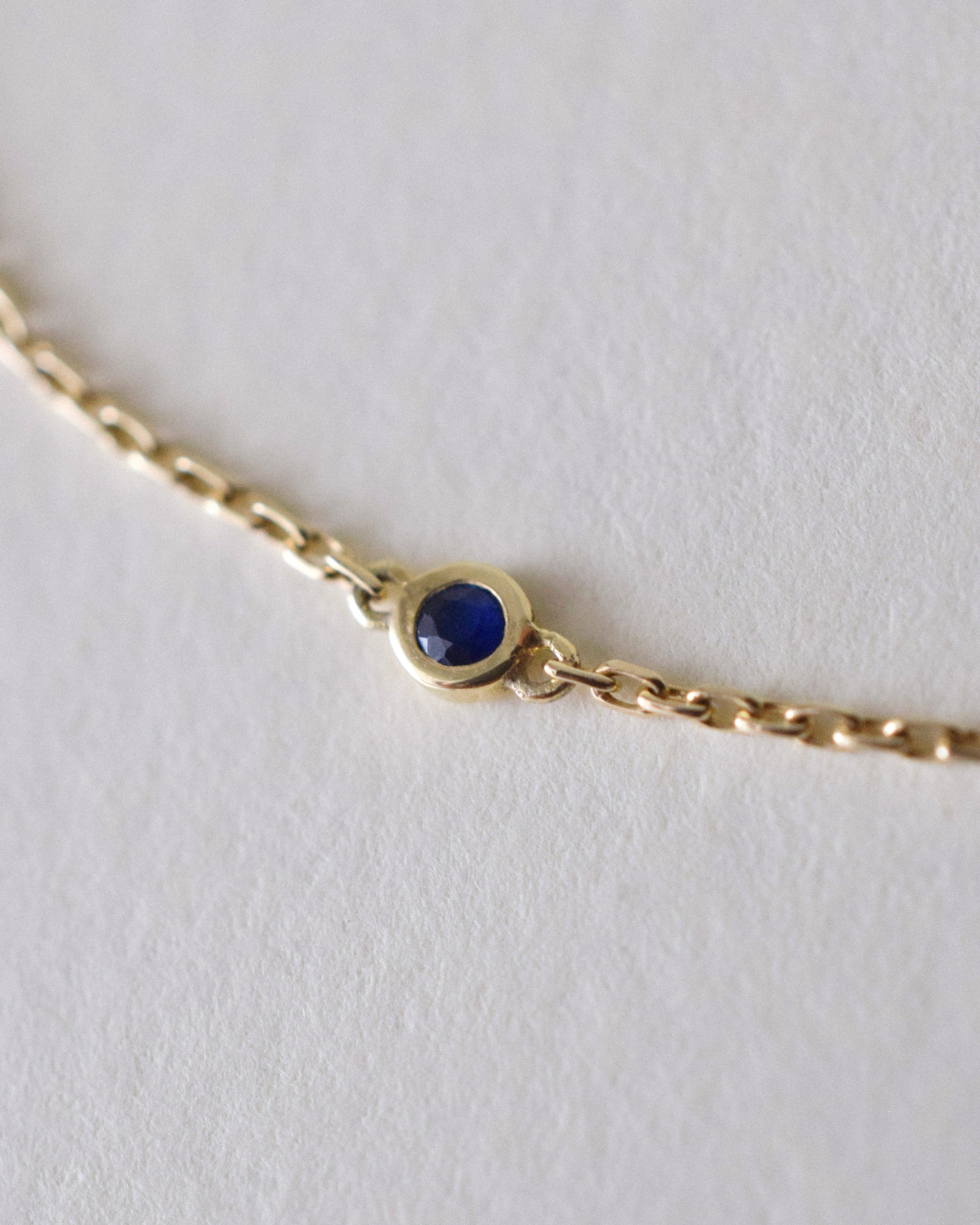 Gold bracelet with a blue sapphire 
gemstone on a light gray background