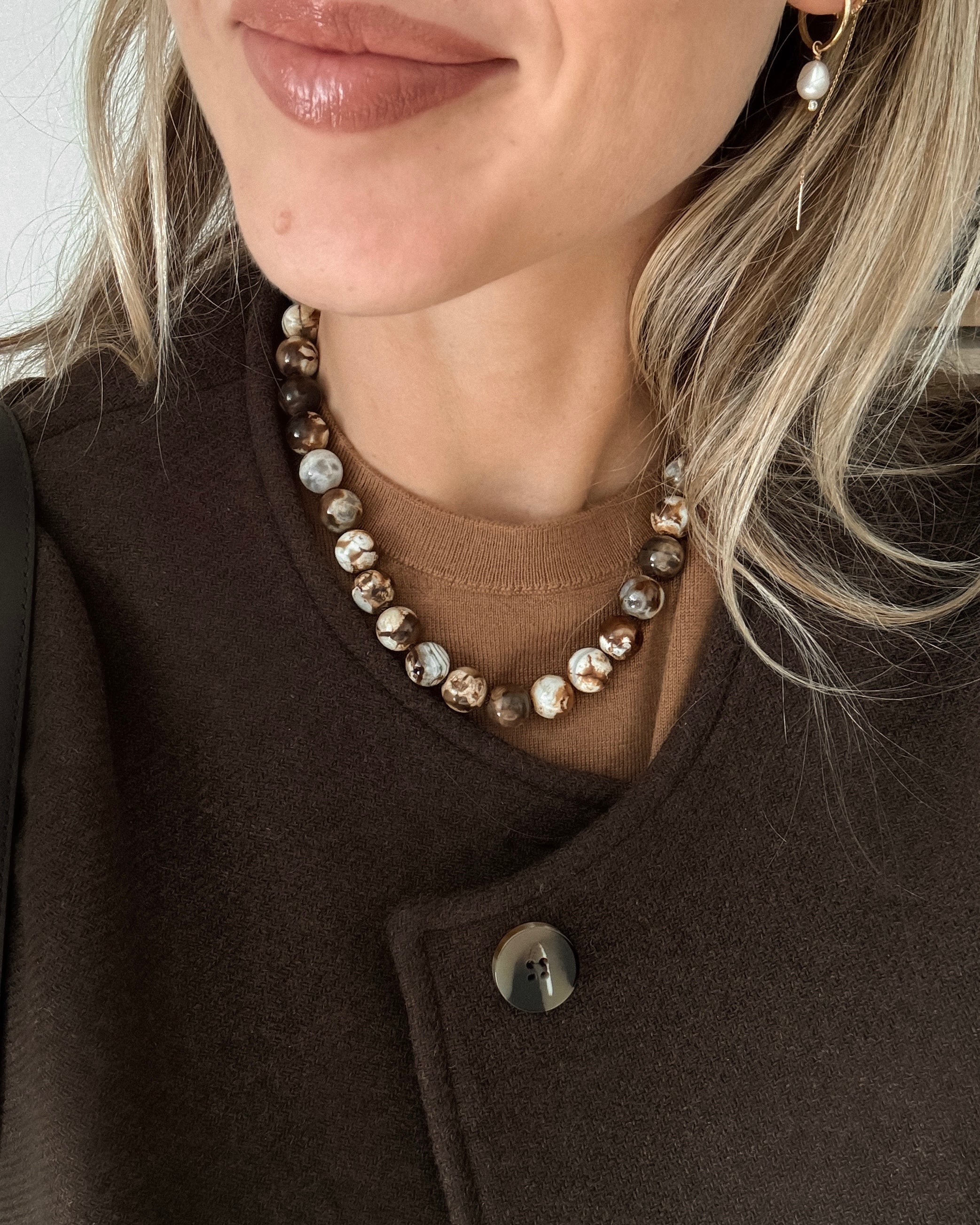 Close-up of a person wearing a brown beaded agate necklace with a neutral background