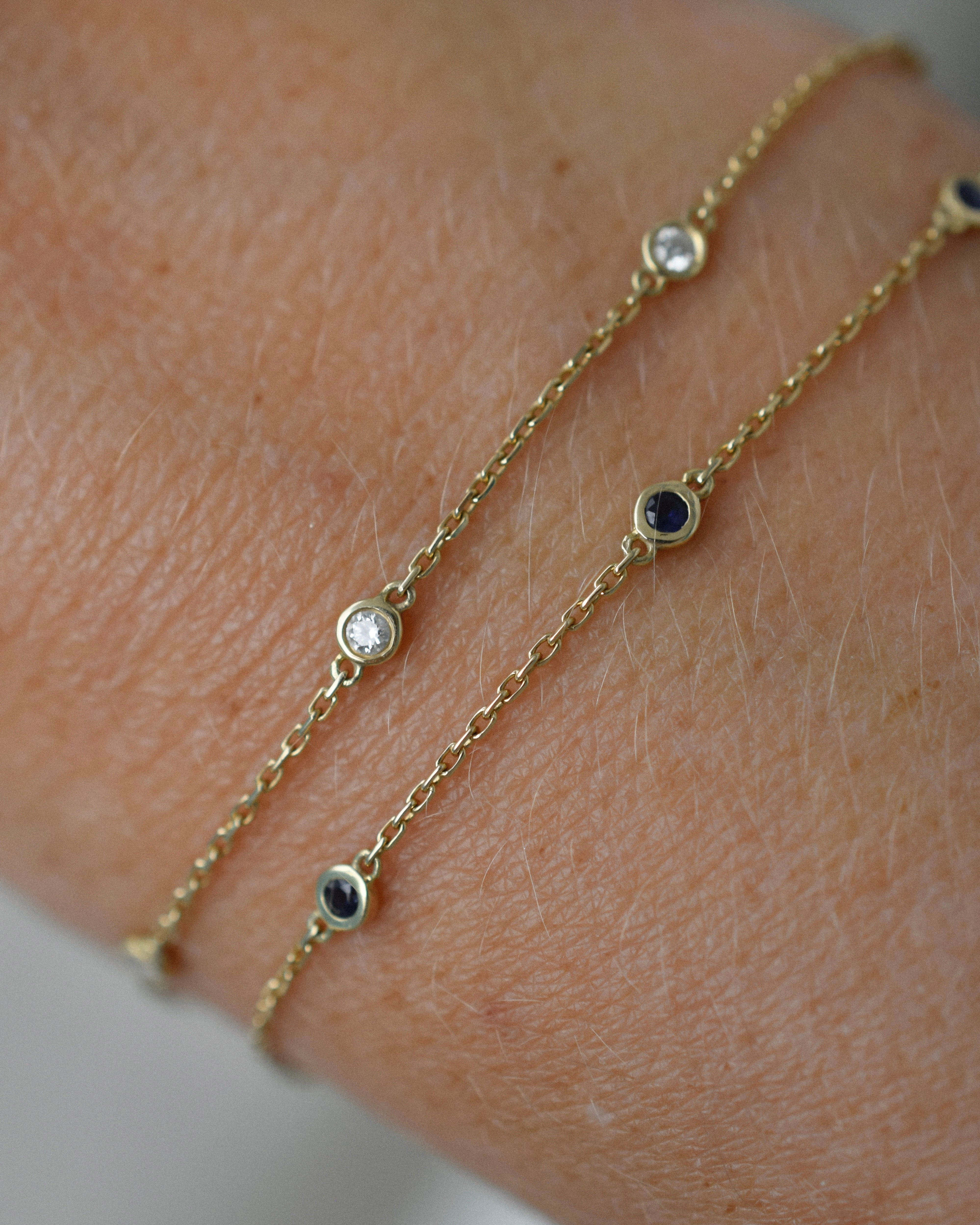 Gold bracelets with diamond and sapphire 
gemstones on a wrist against a neutral background