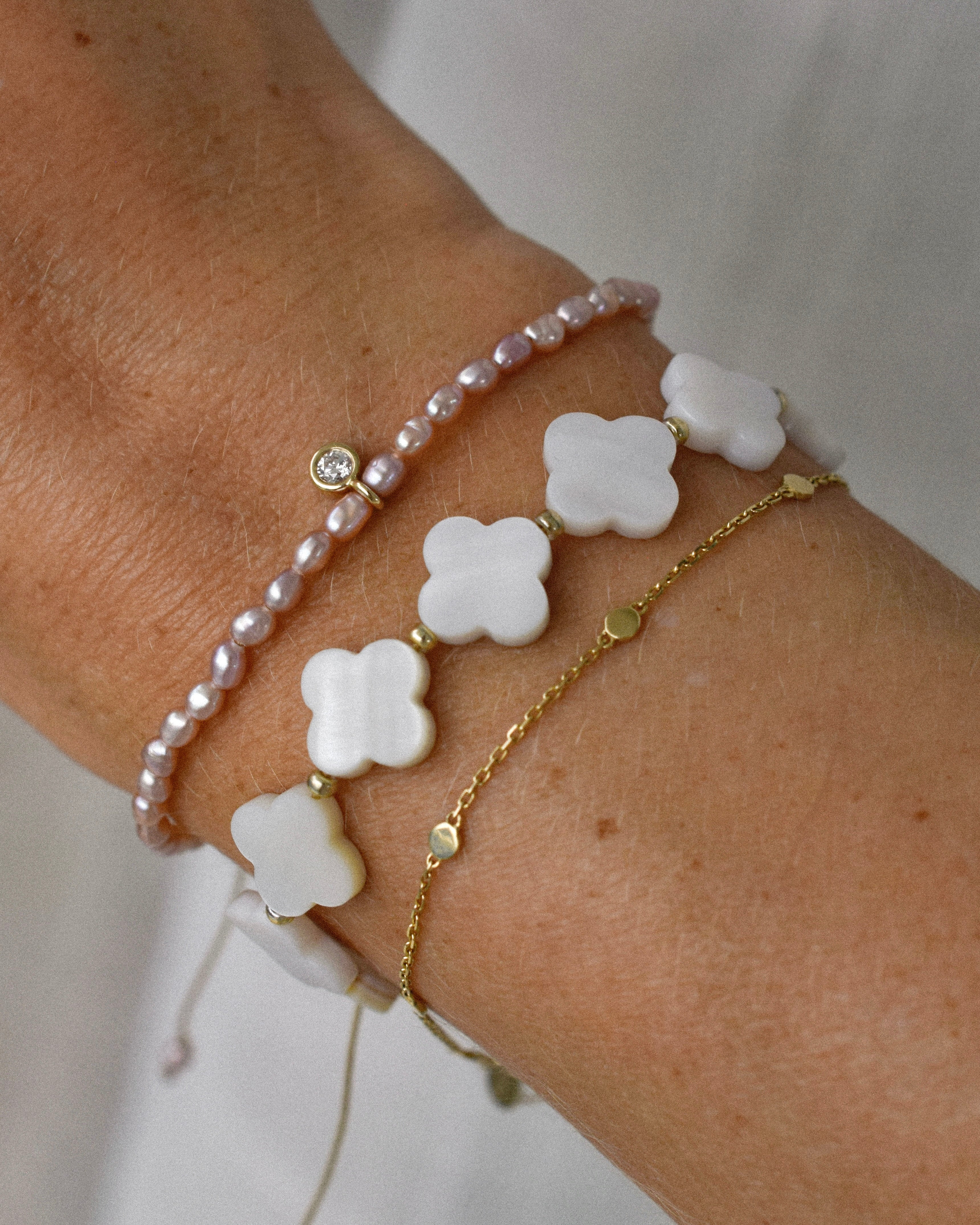 Close-up of a wrist wearing multiple bracelets with clover and pearl designs.