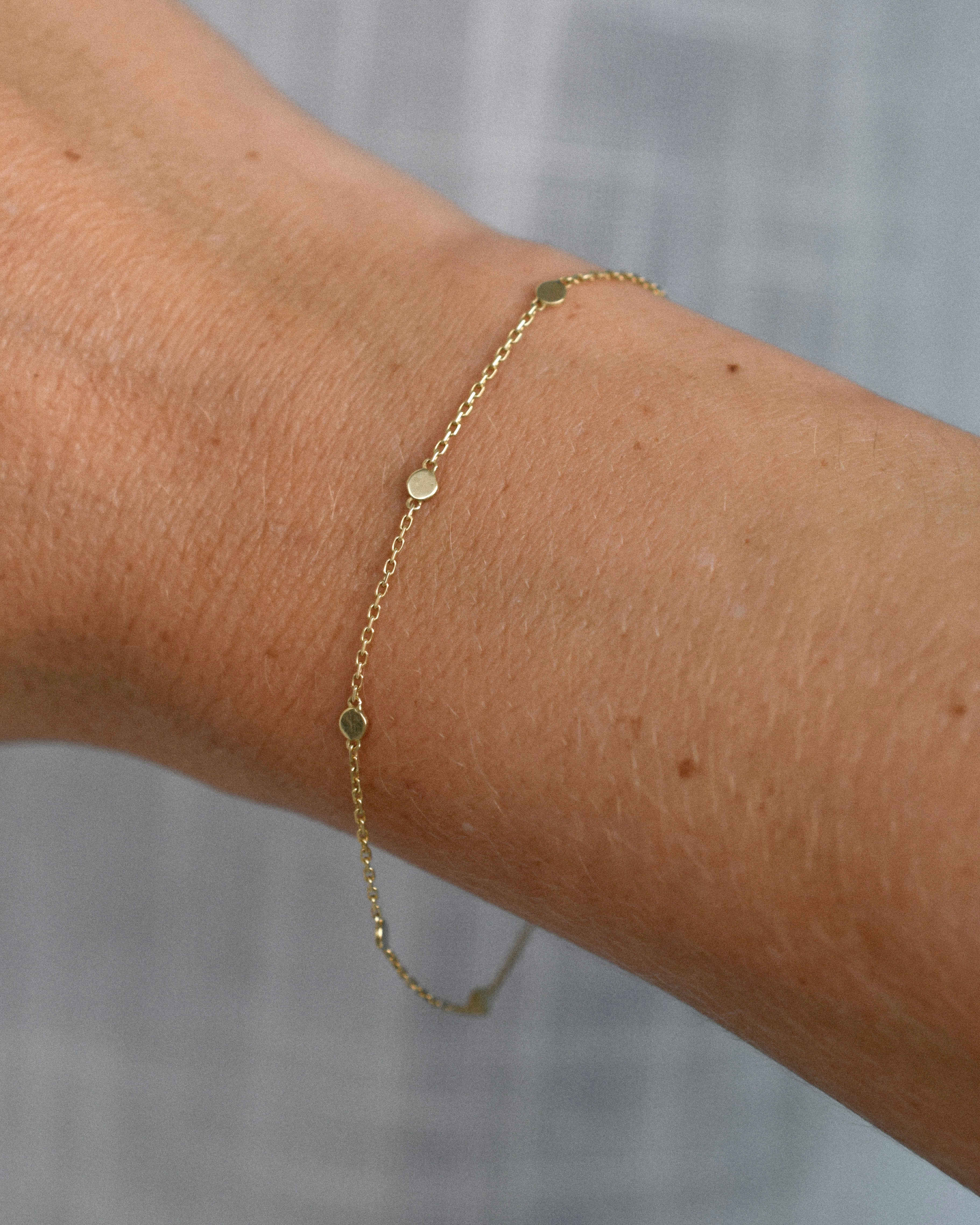 Dainty gold bracelet on a wrist with a plain background
