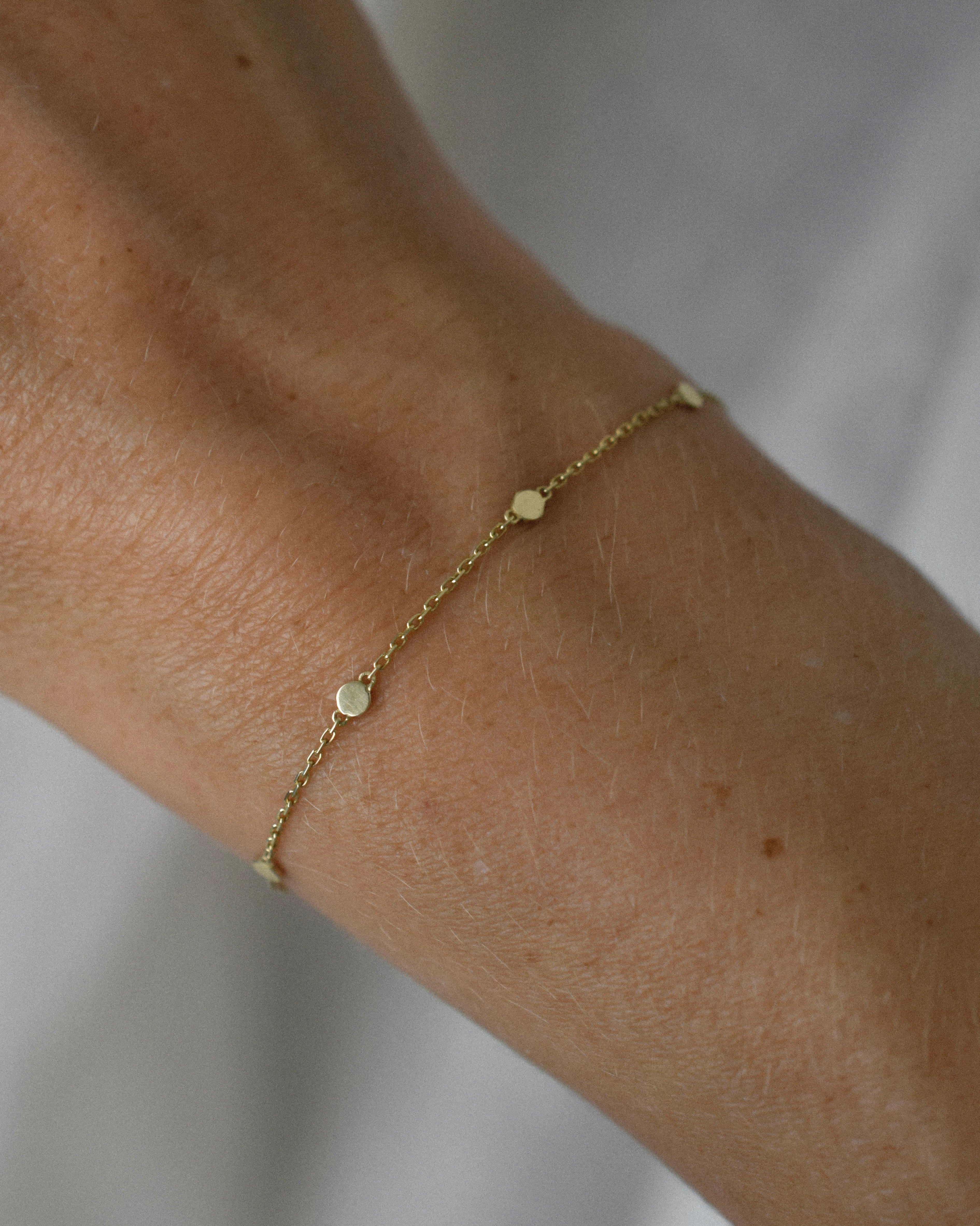 Gold bracelet on a wrist against a neutral background