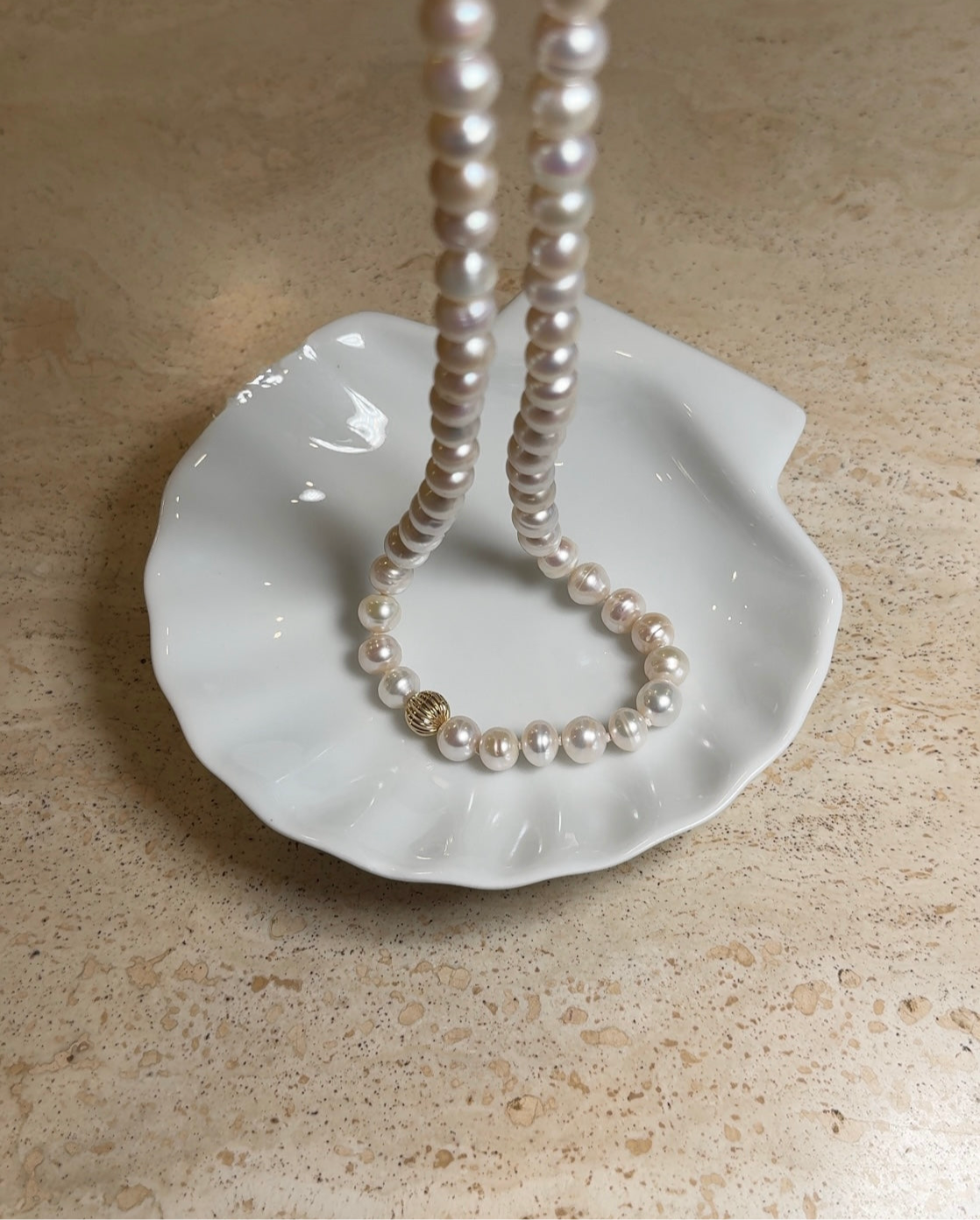 Pearl necklace on a white shell-shaped dish against a beige background