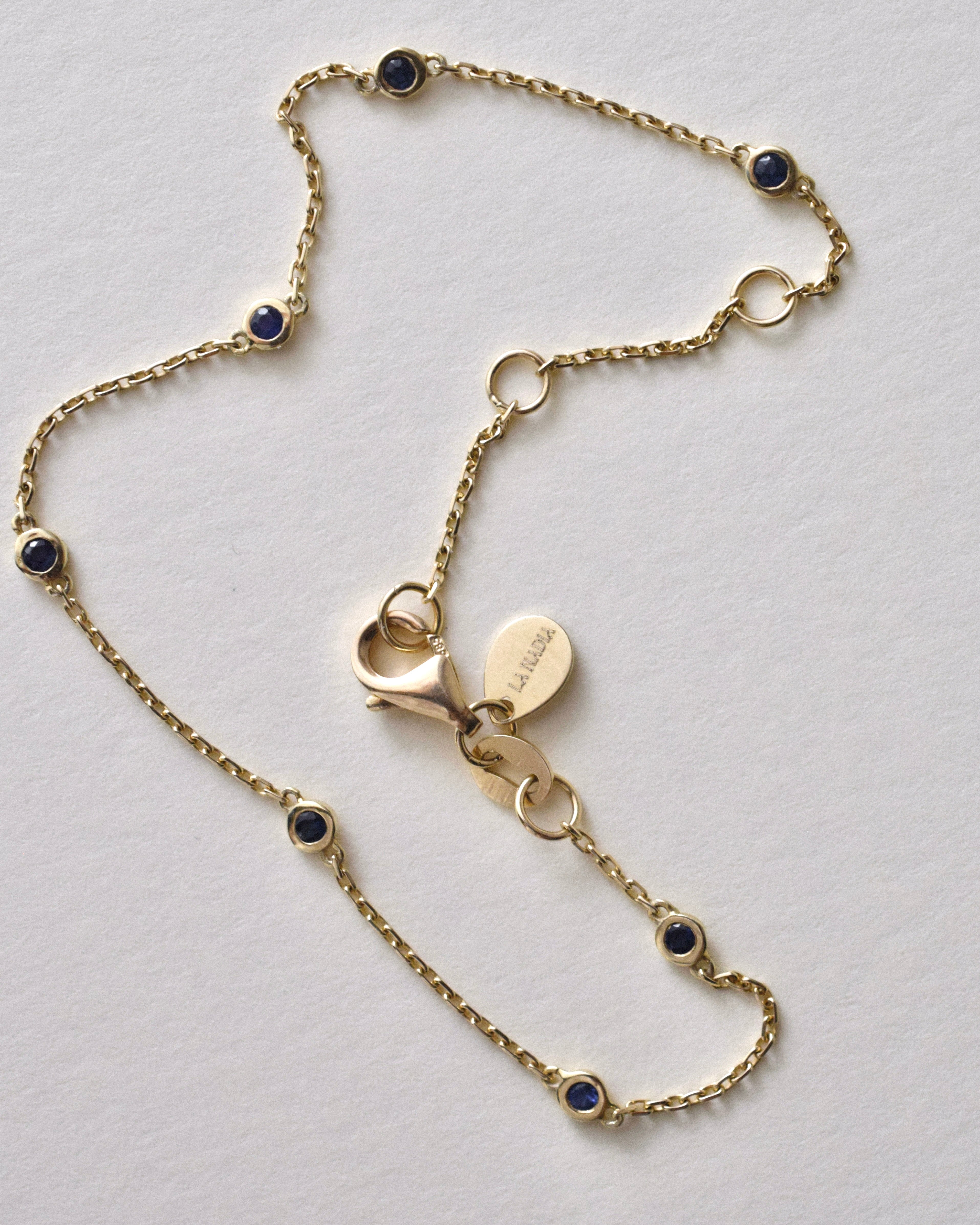 Gold necklace with blue sapphire stones on a light gray background