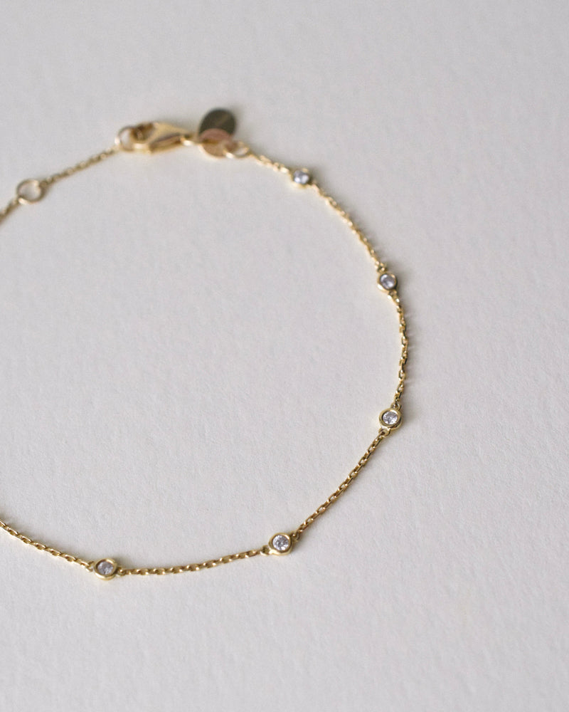 Gold bracelet with small diamonds on a light gray background