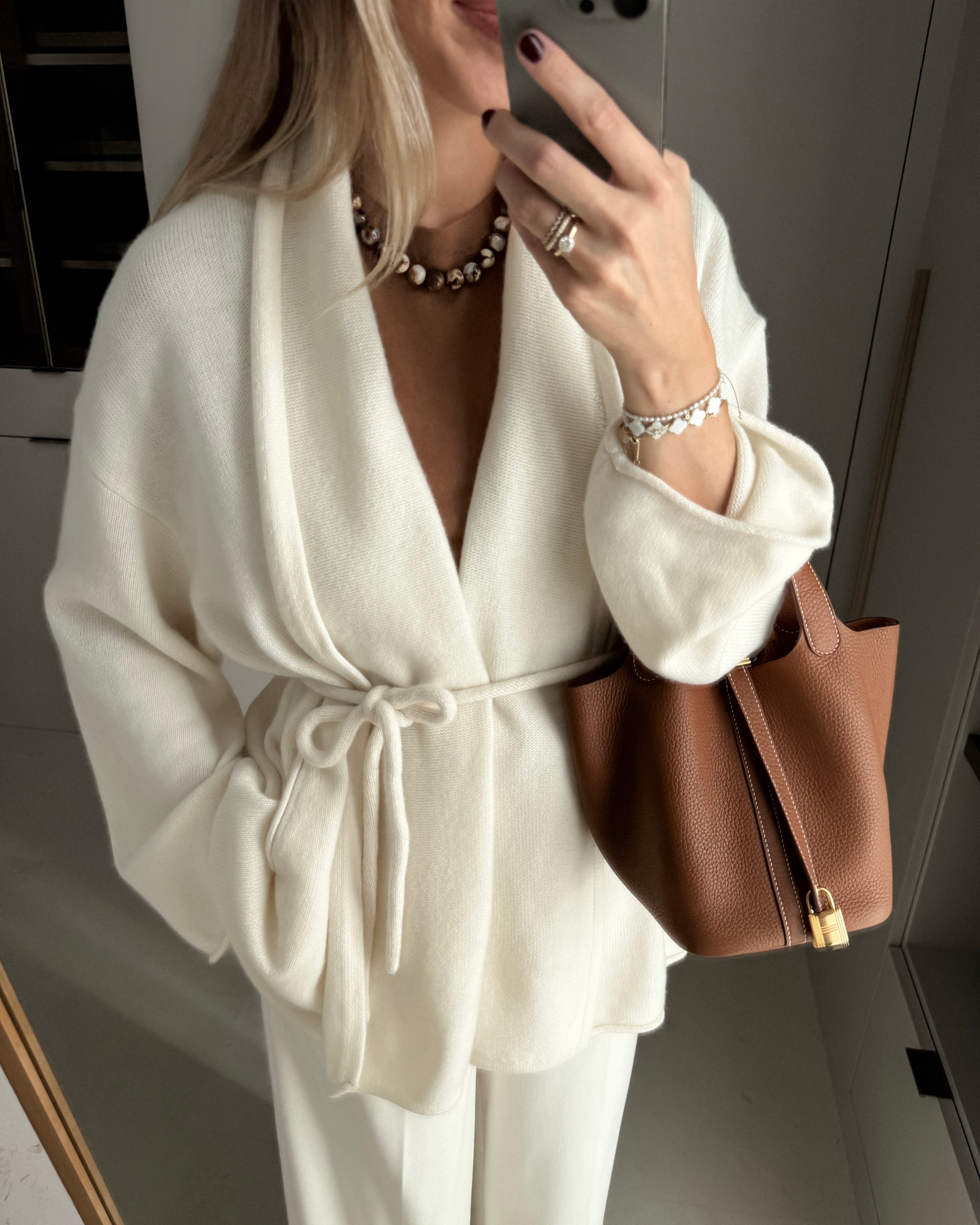 Person wearing a brown beaded agate necklace with a white outfit with a brown handbag, taking a mirror selfie.