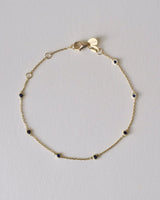 Gold bracelet with small blue sapphire gemstones on a light gray background