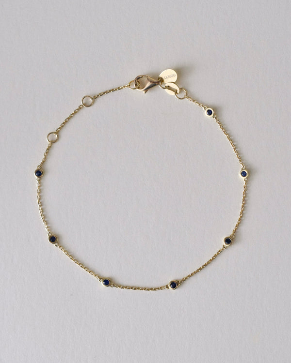 Gold bracelet with small blue sapphire gemstones on a light gray background