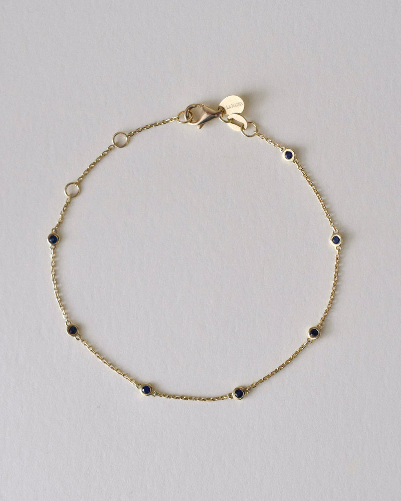 Gold bracelet with small blue sapphire gemstones on a light gray background