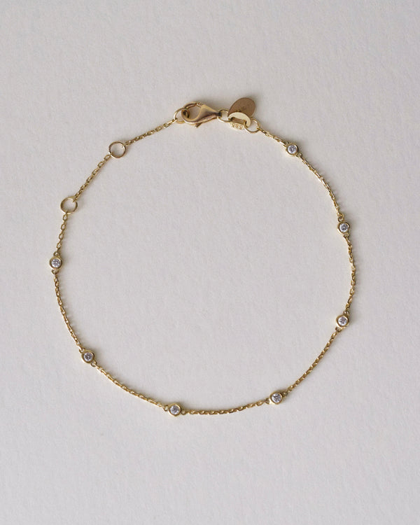 Gold bracelet with 7 diamonds by the yard on a light gray background