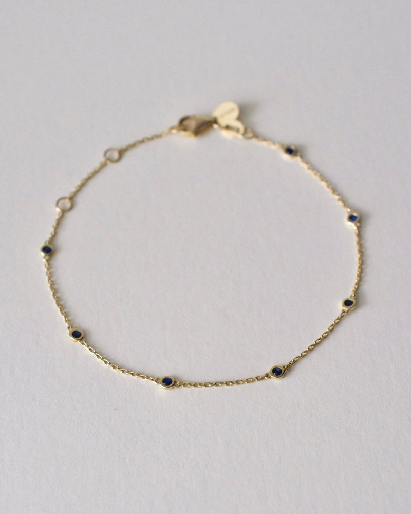 Gold bracelet with small blue sapphire gemstones on a light gray background