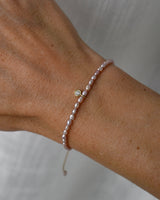 Pearl bracelet with purple pearls and a diamond solitaire charm on a wrist against a neutral background