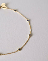 Gold bracelet with small blue sapphire stones on a light gray background