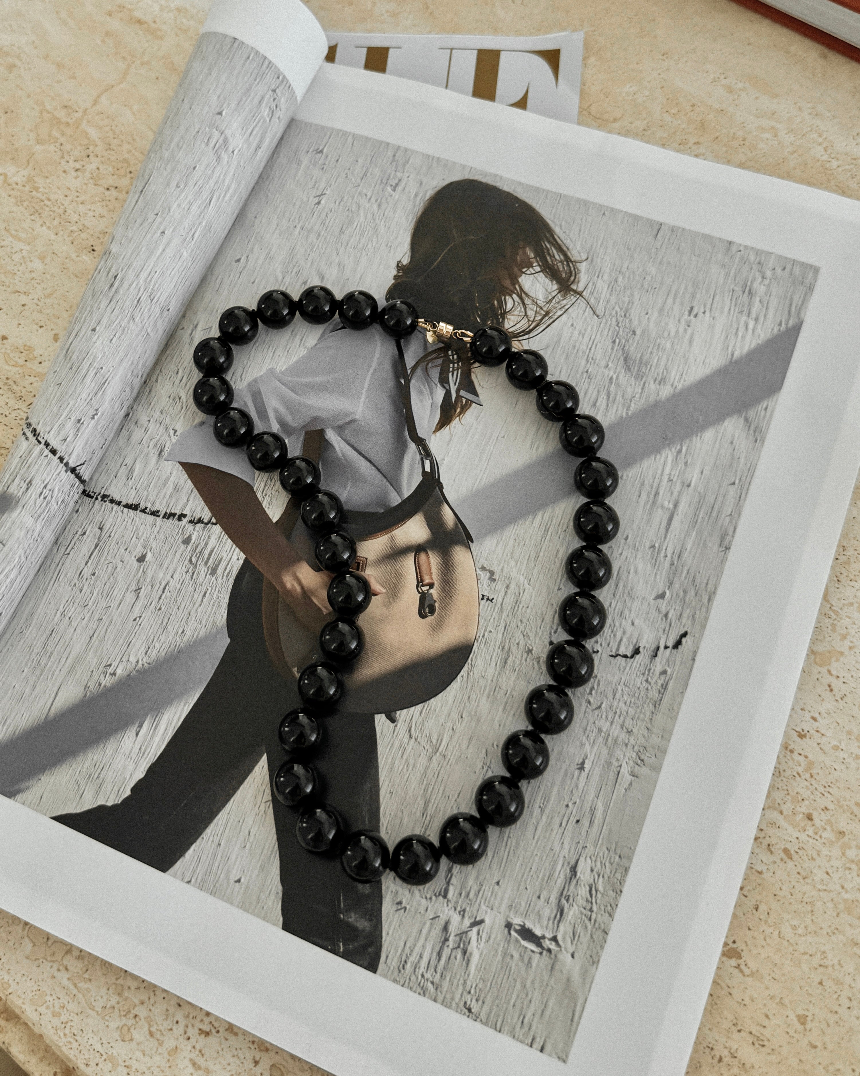 Black beaded onyx stone necklace on a magazine with a blurred silhouette of a person holding a bag.