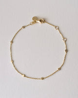 Gold bracelet with seven coin-shaped charms, lobster clasp and jewelry tag on a light gray background