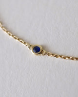 Gold bracelet with a blue sapphire 
gemstone on a light gray background