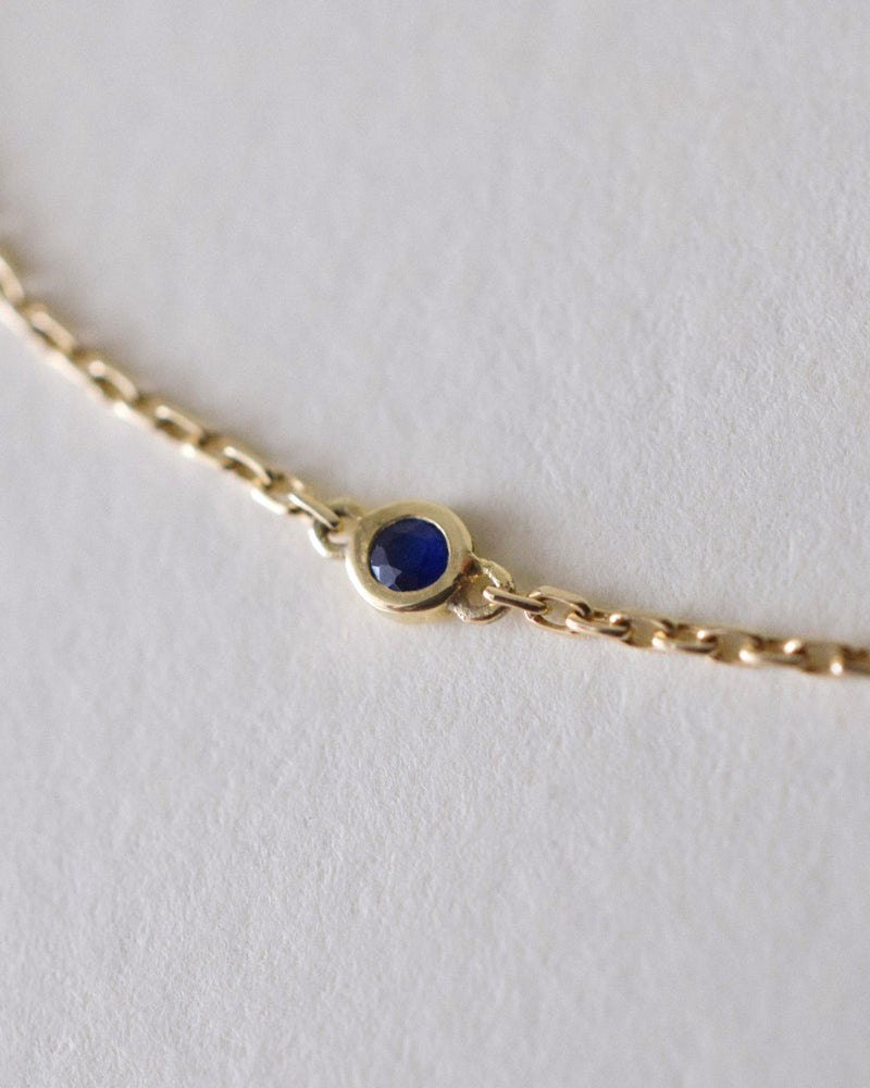 Gold bracelet with a blue sapphire 
gemstone on a light gray background