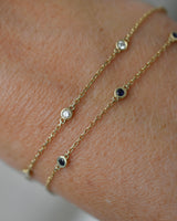 Gold bracelets with diamond and sapphire 
gemstones on a wrist against a neutral background