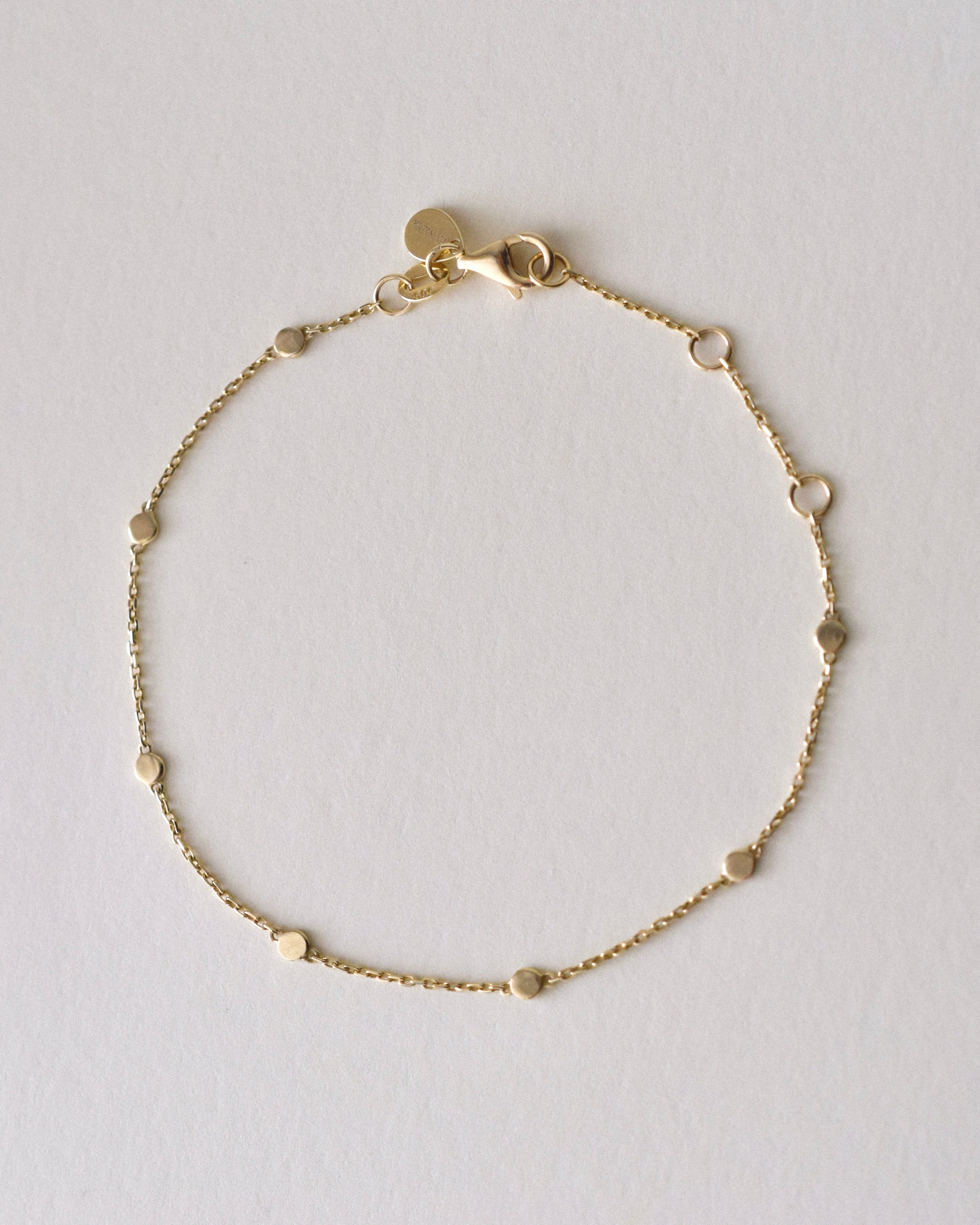 Gold bracelet with seven coin-shaped charms, lobster clasp and jewelry tag on a light gray background
