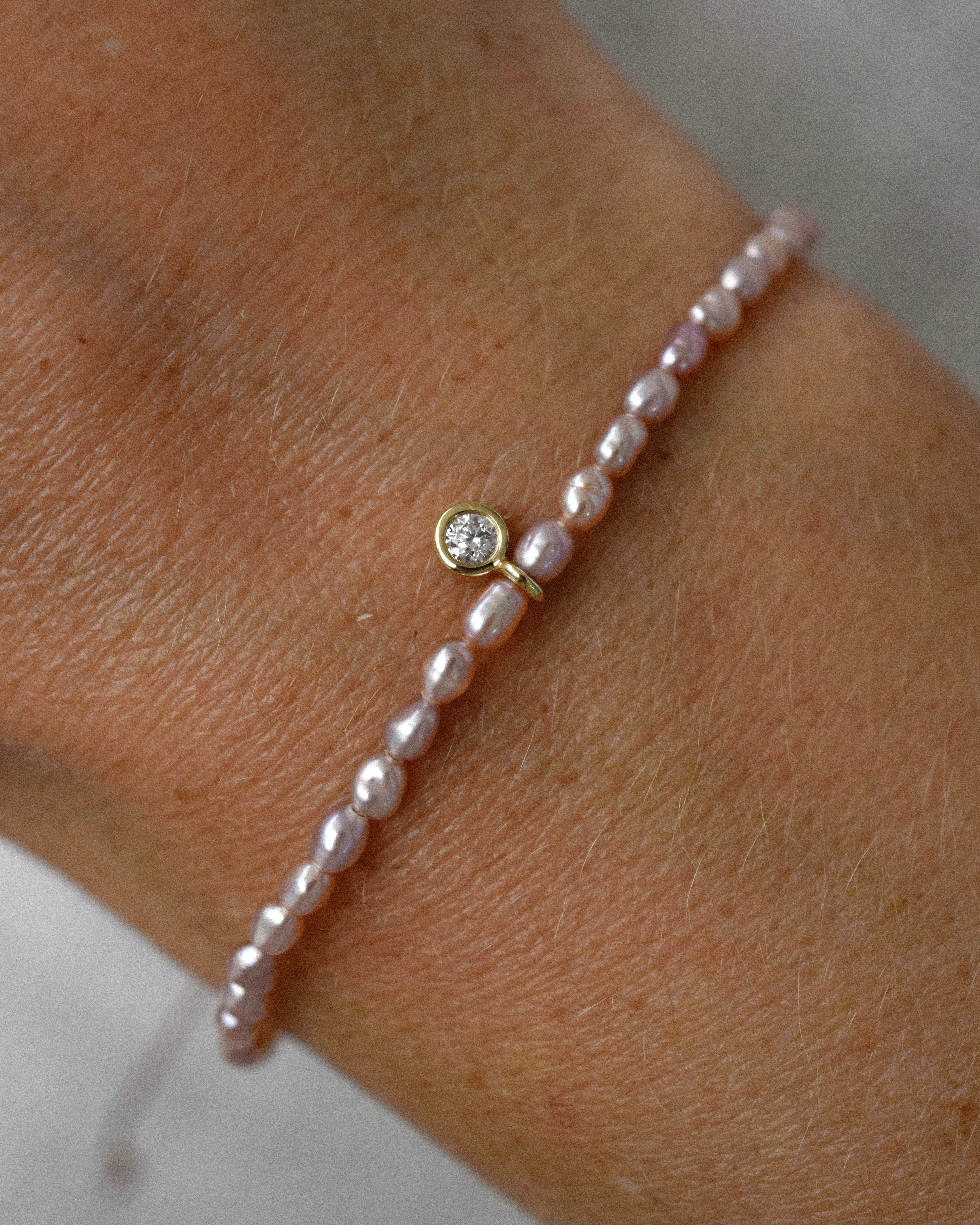 Pearl bracelet with purple pearls and a diamond solitaire charm on a wrist against a neutral background